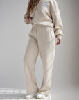 Angled view of a woman wearing Heather Eggshell wide leg sweatpants with a coordinating hoodie.