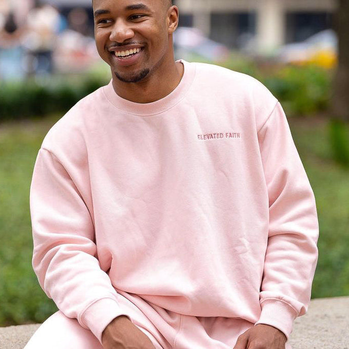Man wearing a pink sweatshirt sitting outdoors with a blurred background