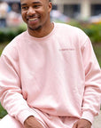 Man wearing a pink sweatshirt sitting outdoors with a blurred background