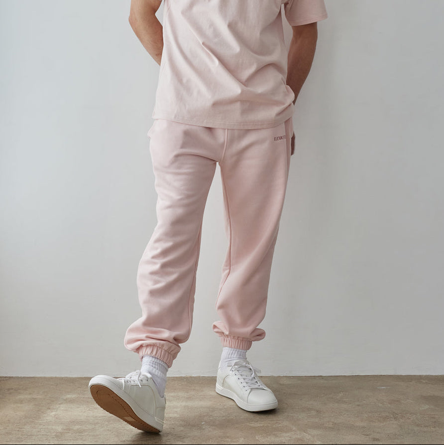 Man wearing a pink outfit with white sneakers against a plain background