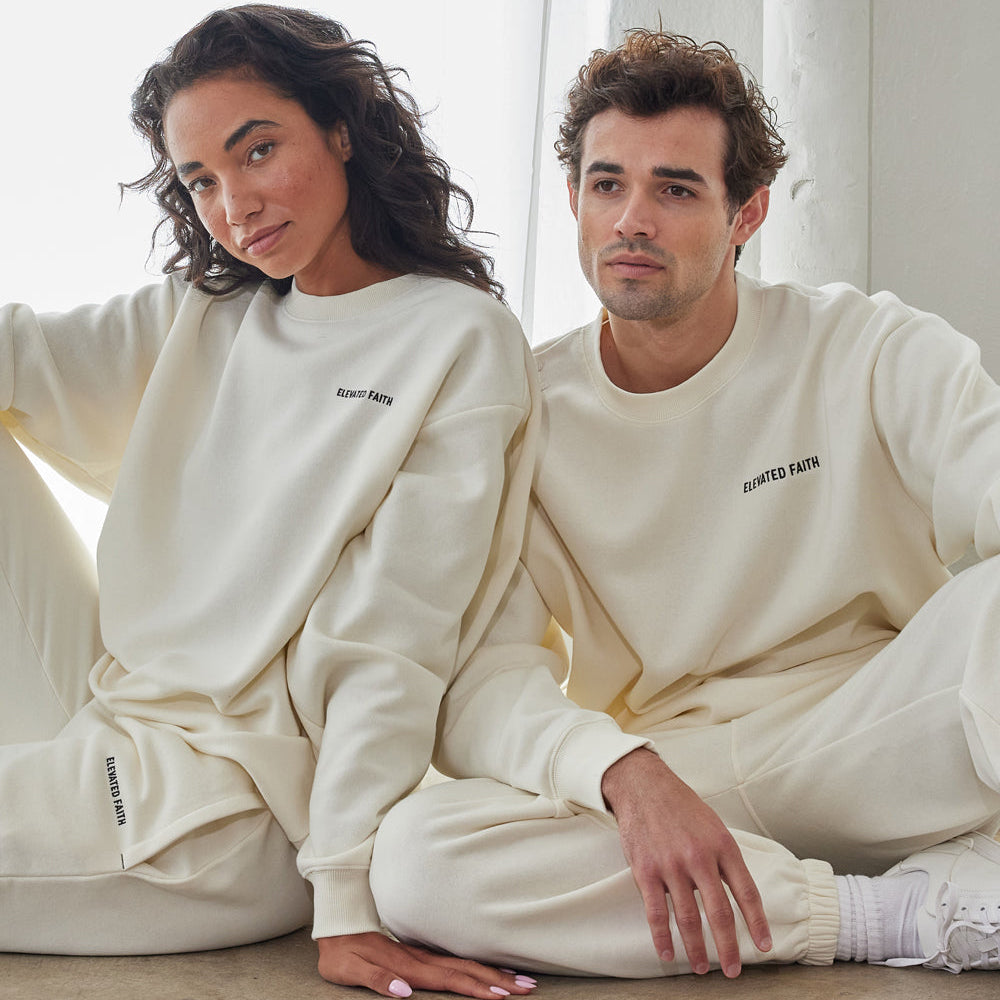 Two people wearing matching white sweatshirts and pants sitting on a light-colored floor.