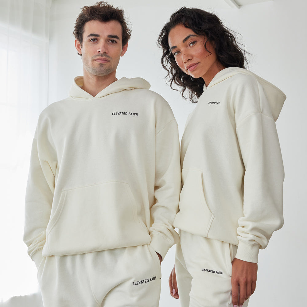 Two people wearing matching cream-colored hoodies and pants with a brand logo.