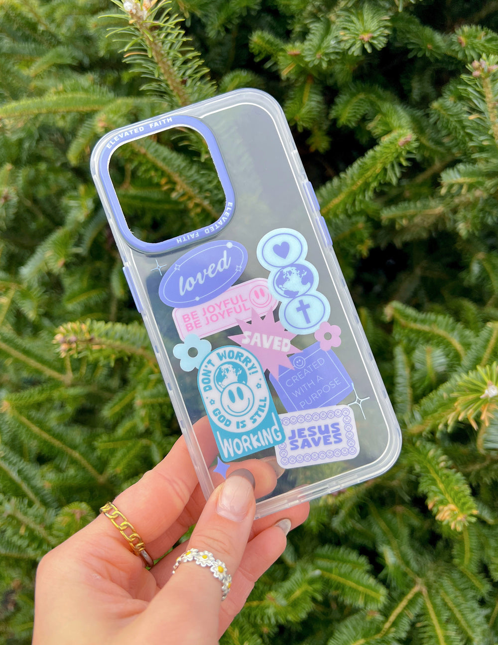 Be Joyful iPhone Case held against green foliage, showing pastel faith-inspired graphics and the camera opening