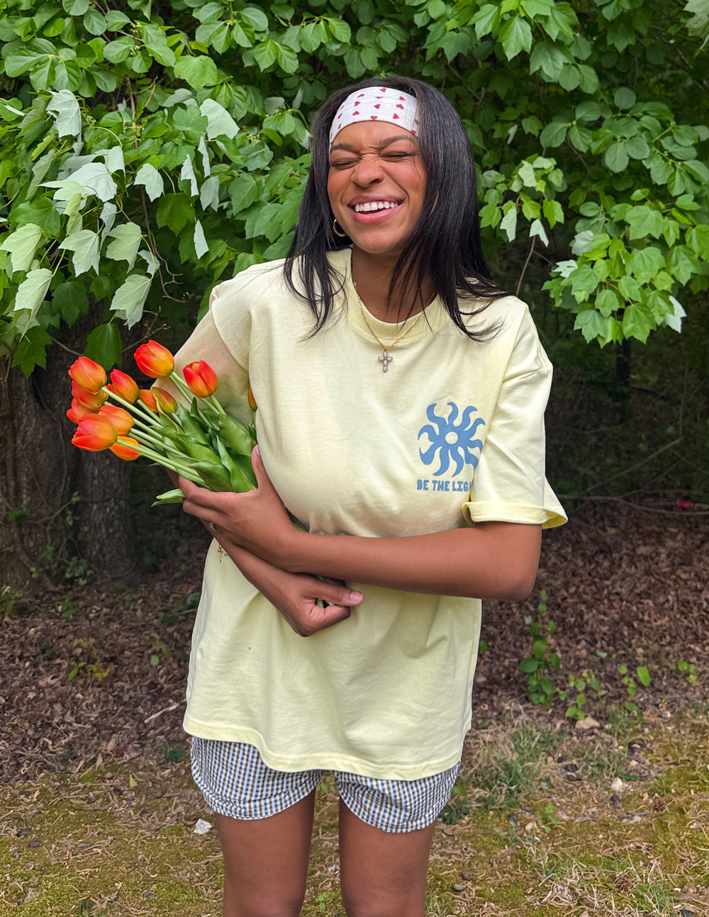 Model holding orange tulips while wearing the yellow Be the Light Unisex Tee with white shorts