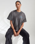 Front view of a seated model wearing the boxy Believe in Miracles Heavyweight Tee in Lamp Black