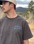 Model wearing the Lamp Black Believe in Miracles tee with a cap outdoors
