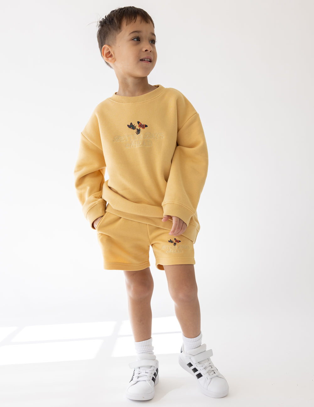 Child wearing the New Wheat yellow Better Days Butterfly crewneck sweatshirt with coordinating shorts.