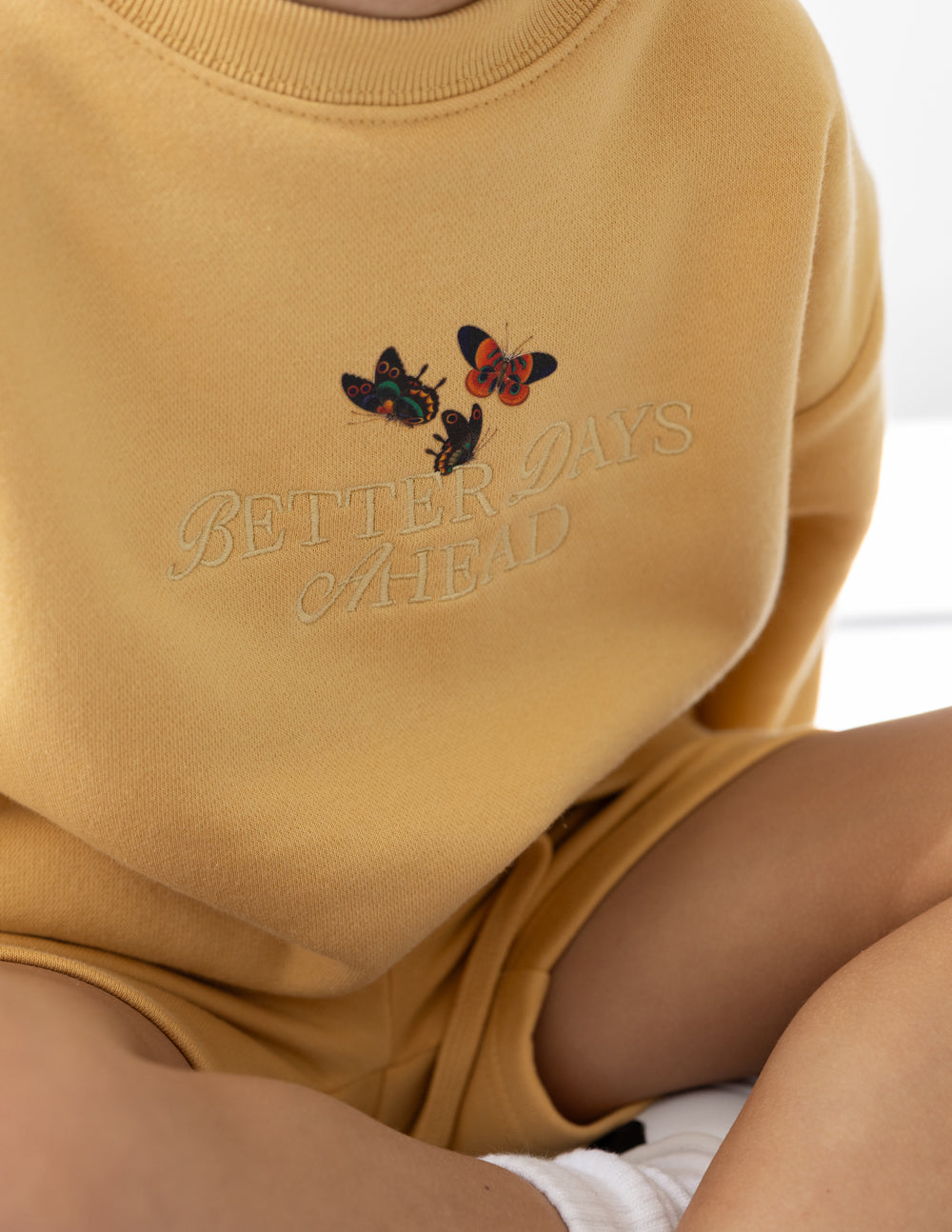 Close-up of colorful butterflies and Better Days Ahead embroidery on the New Wheat kids’ sweatshirt.
