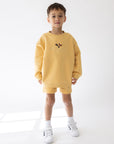 Front view of a child wearing the oversized yellow butterfly sweatshirt with white socks and sneakers.