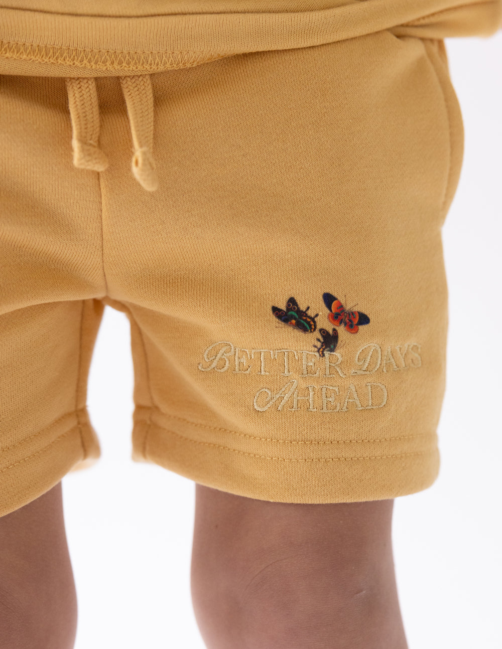Close-up of colorful butterflies and Better Days Ahead lettering near the hem of the yellow shorts.