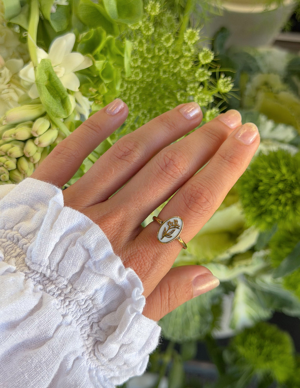 Hand wearing the Bloom Again Enamel Ring against green foliage and white flowers