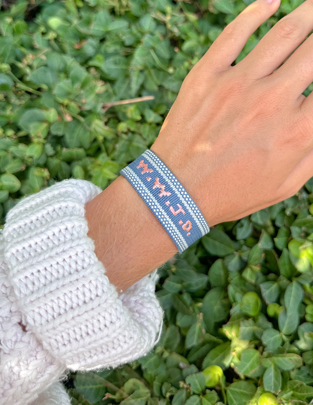 Moonlight Navy WWJD bracelet worn on a wrist against green foliage.