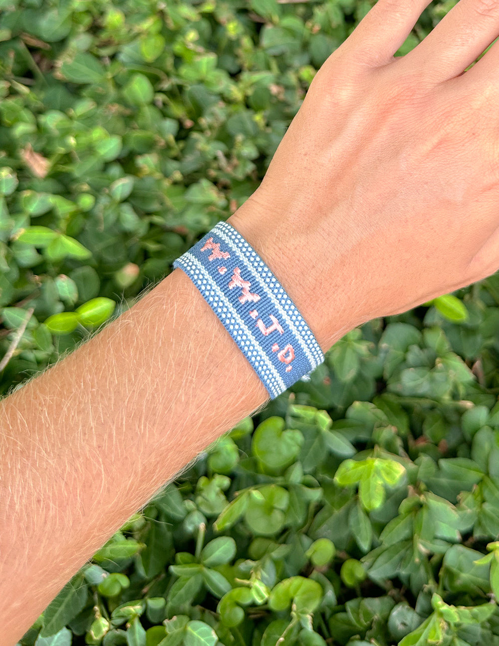 Close-up of the blue WWJD embroidered bracelet worn on a wrist outdoors.