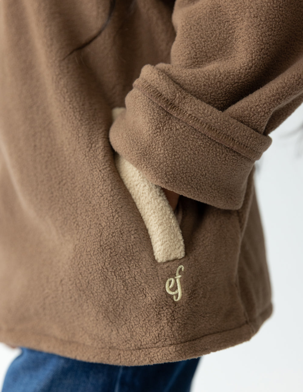 Close-up of the Chestnut fleece pullover showing a cream pocket zipper and embroidered logo.