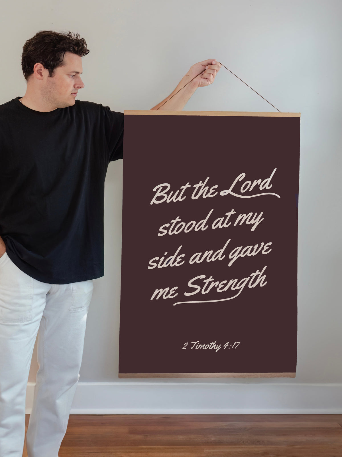 Man holding But the Lord Stood 24 by 36-inch Scripture wall art with a wooden hanging banner