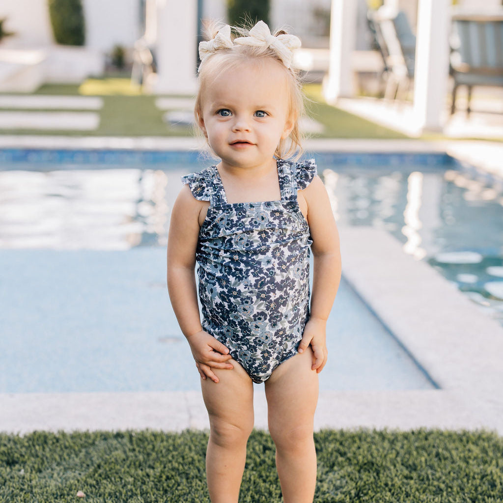 Child in a floral swimsuit standing by a pool