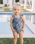 Child in a floral swimsuit standing by a pool
