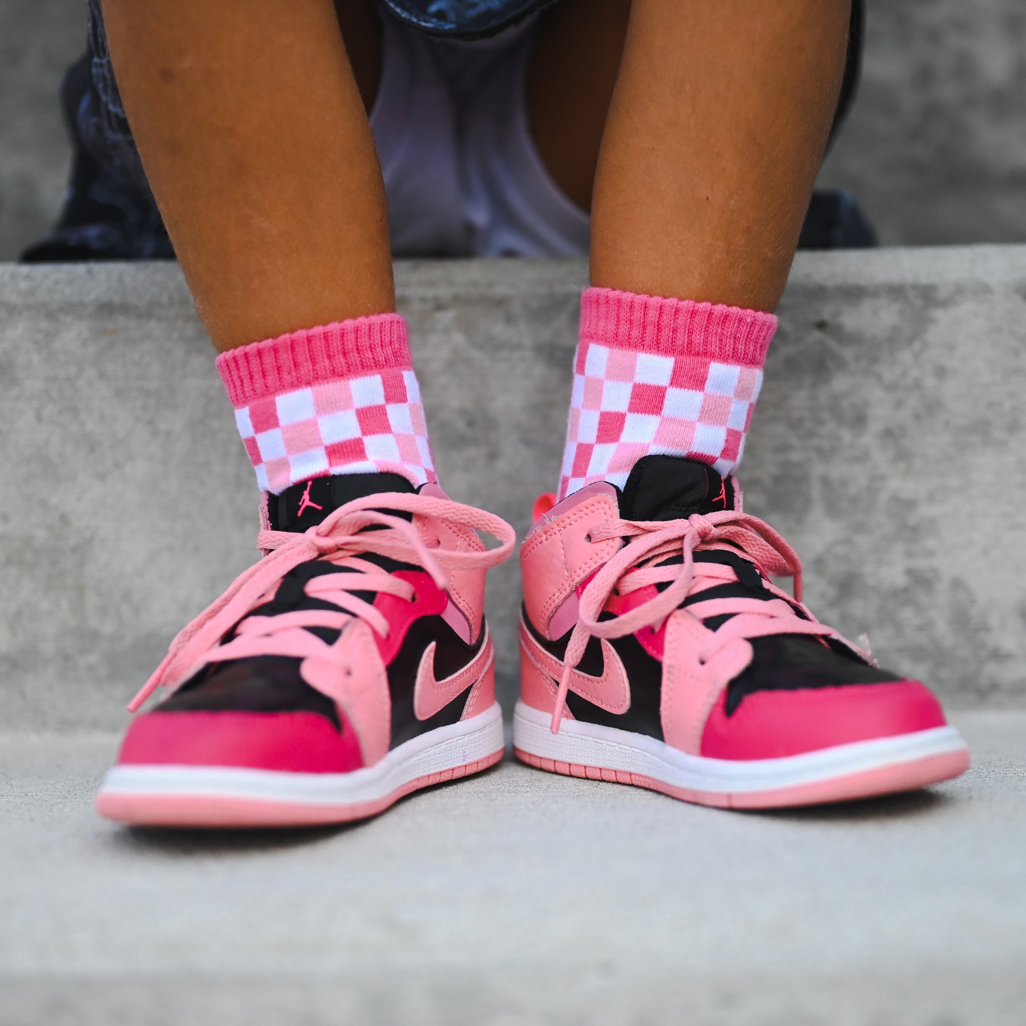 Pink and black sneakers with checkered socks worn by a person.