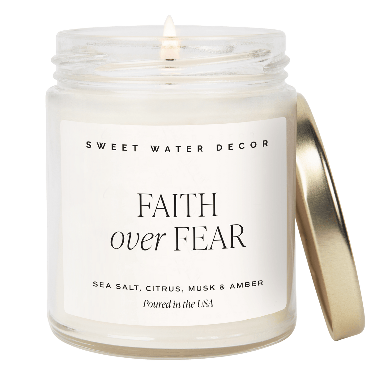 Faith Over Fear candle in a clear glass jar with a cream label and gold-tone lid leaning beside it
