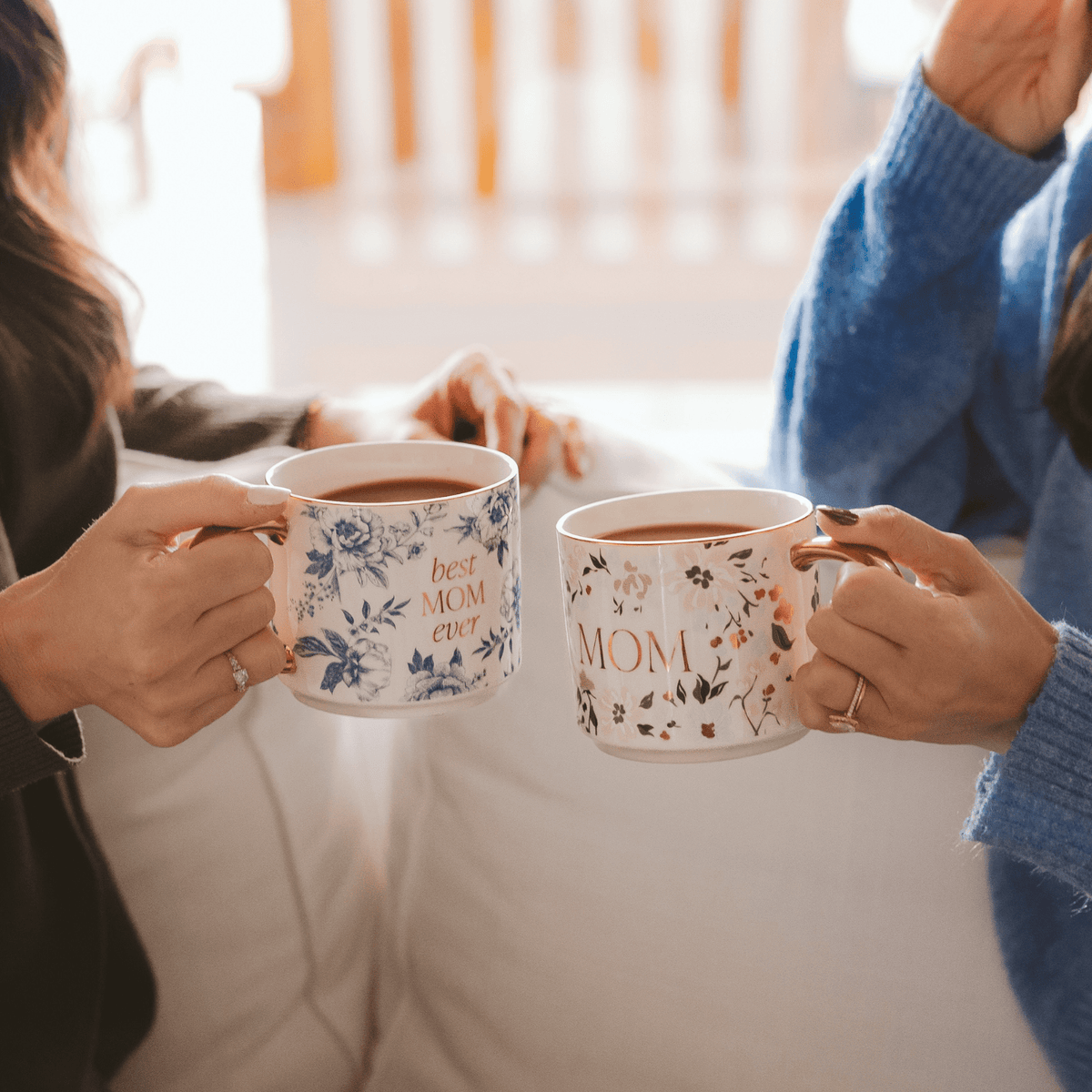 Two people holding floral gold handle mugs, including the blue Best Mom Ever design