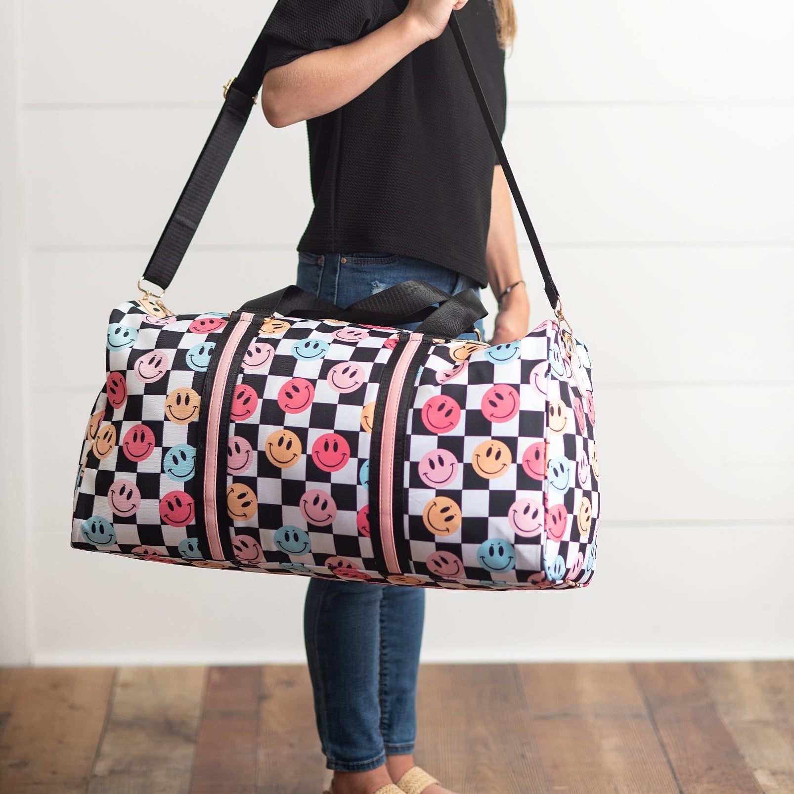 Person holding a checkered duffel bag with smiley face patterns against a white wall.
