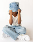 Child seated wearing a light-wash Child of God denim bucket hat