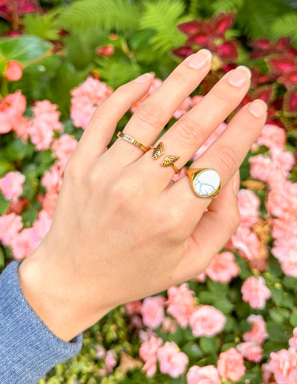 Hand wearing the Howlite Stone Gold-Tone Ring with other rings in front of pink flowers