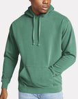 Male model wearing a seafoam green Comfort Colors garment-dyed hoodie, featuring a relaxed fit and front pocket — ideal for custom printing by Lumiere Vive.