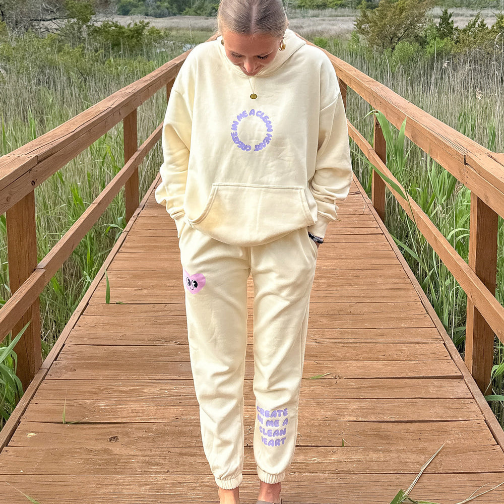 Person wearing a beige hoodie and pants on a wooden boardwalk with nature in the background