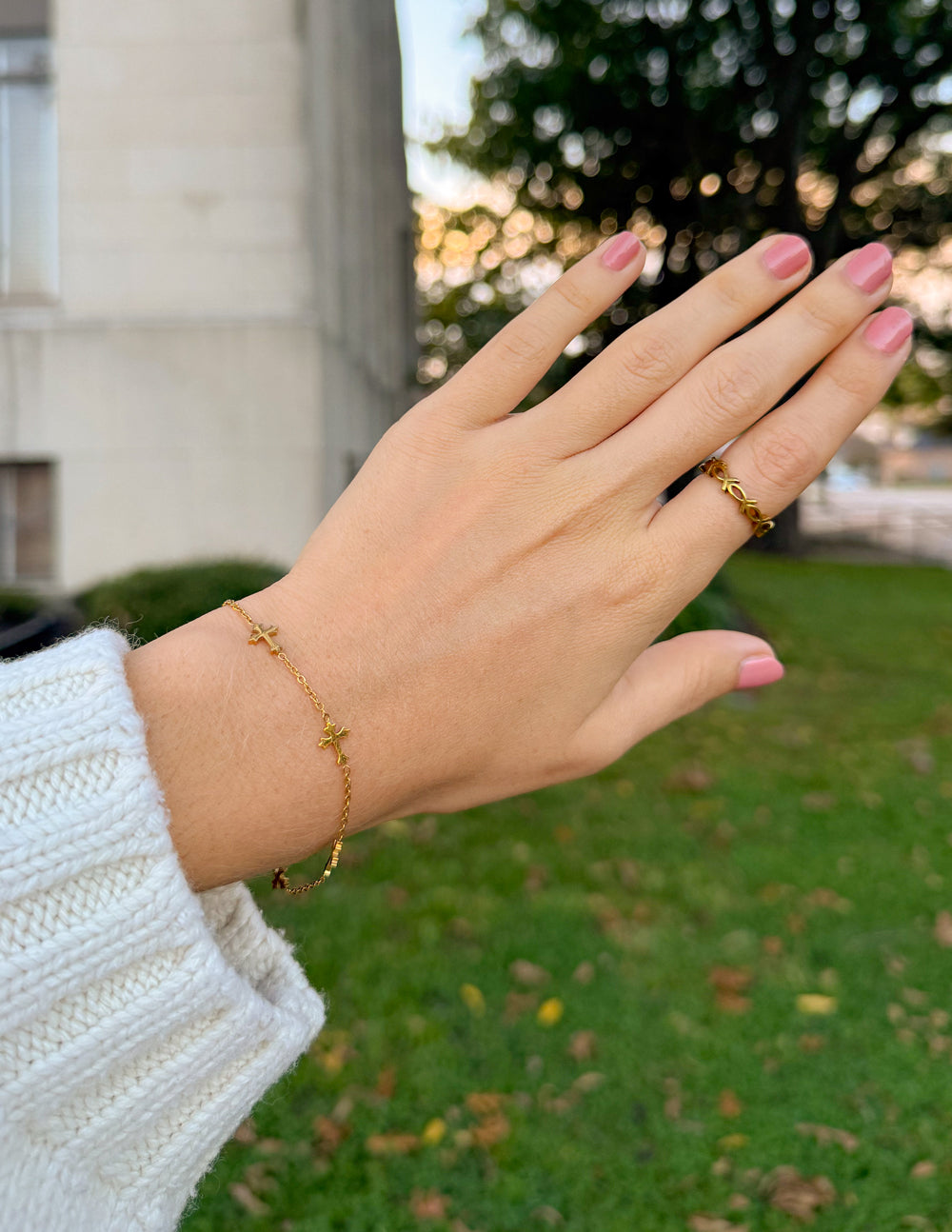 Close-up of gold-tone cross bracelet worn beside evergreen foliage