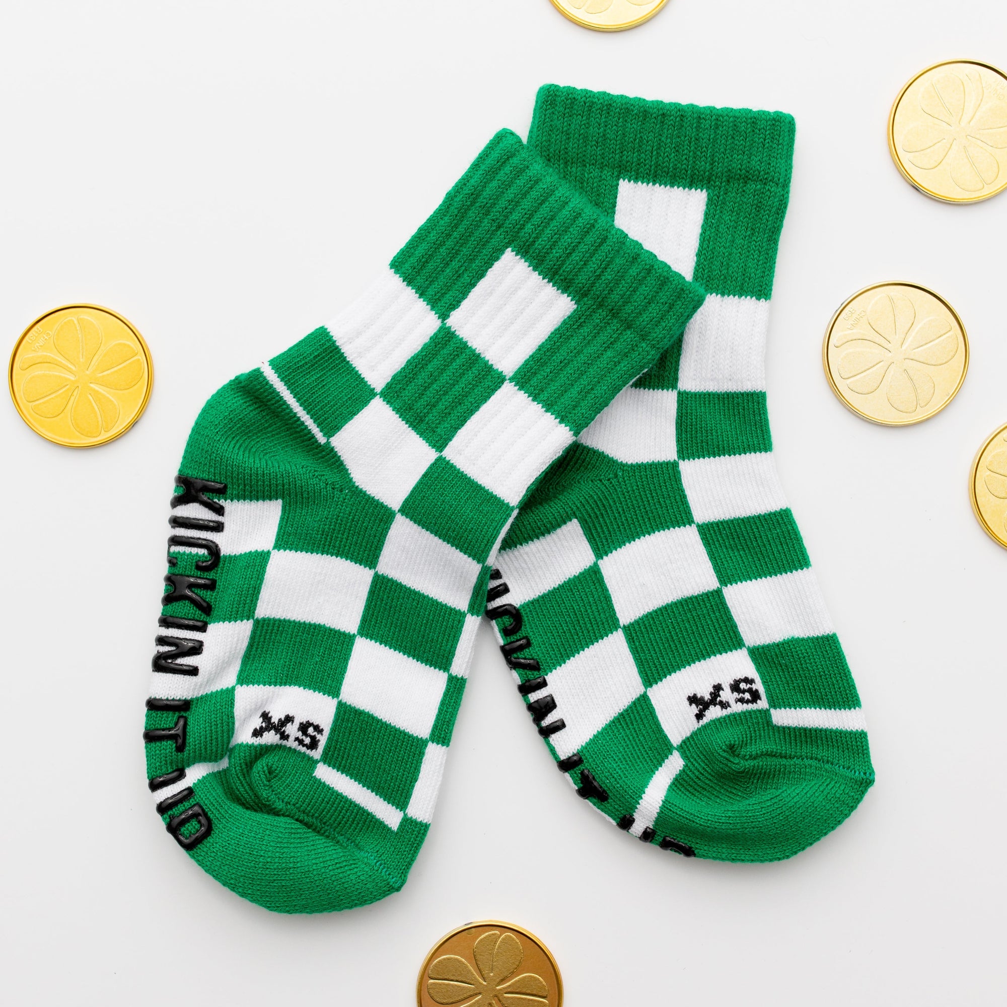 Green and white checkered socks with 'XS' branding on a light background with gold coins.