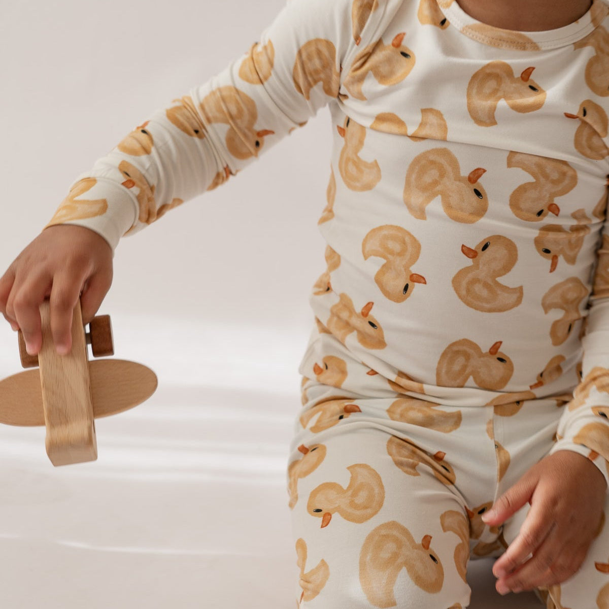 Child wearing a onesie with duck pattern holding a wooden toy on a white background