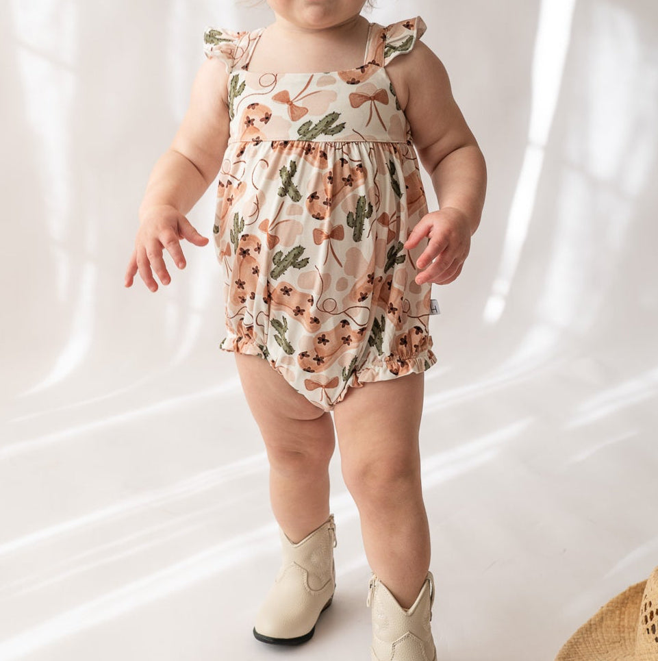 Baby wearing a floral romper and white boots on a plain background