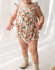 Baby wearing a floral romper and white boots on a plain background