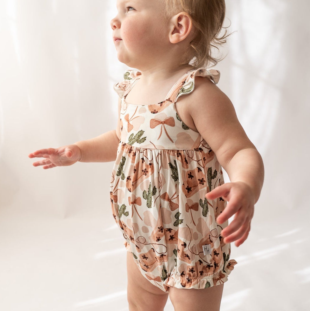 Baby wearing a floral romper and white boots on a plain background