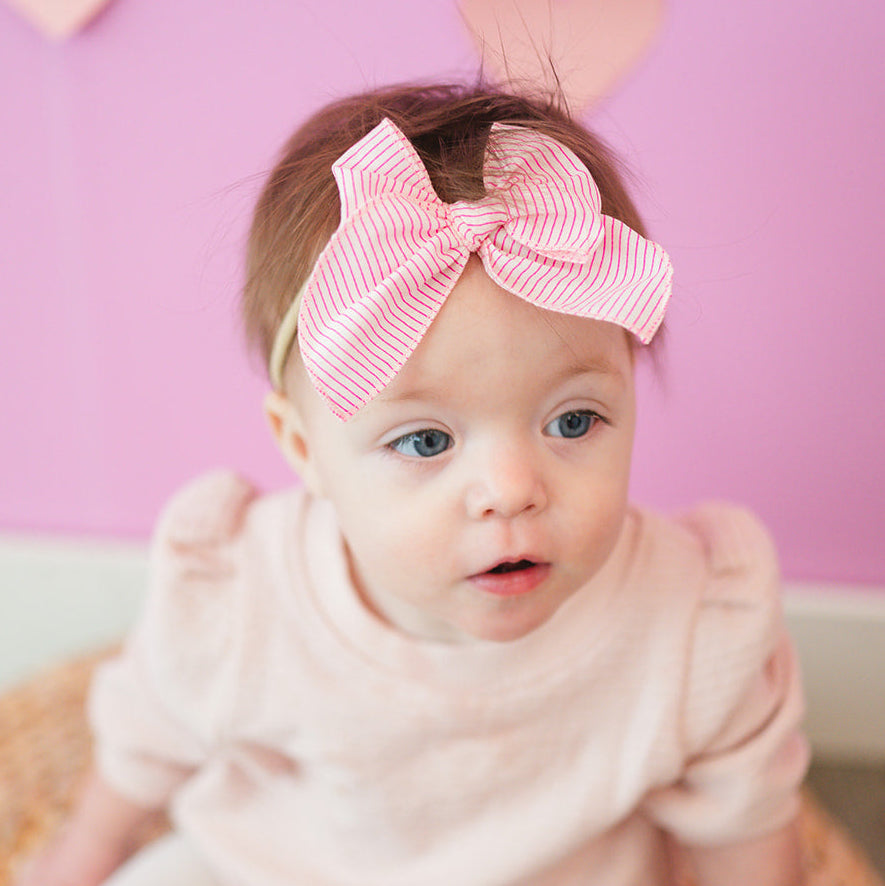 Baby wearing a pink outfit and headband with a heart-shaped background