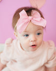 Baby wearing a pink outfit and headband with a heart-shaped background