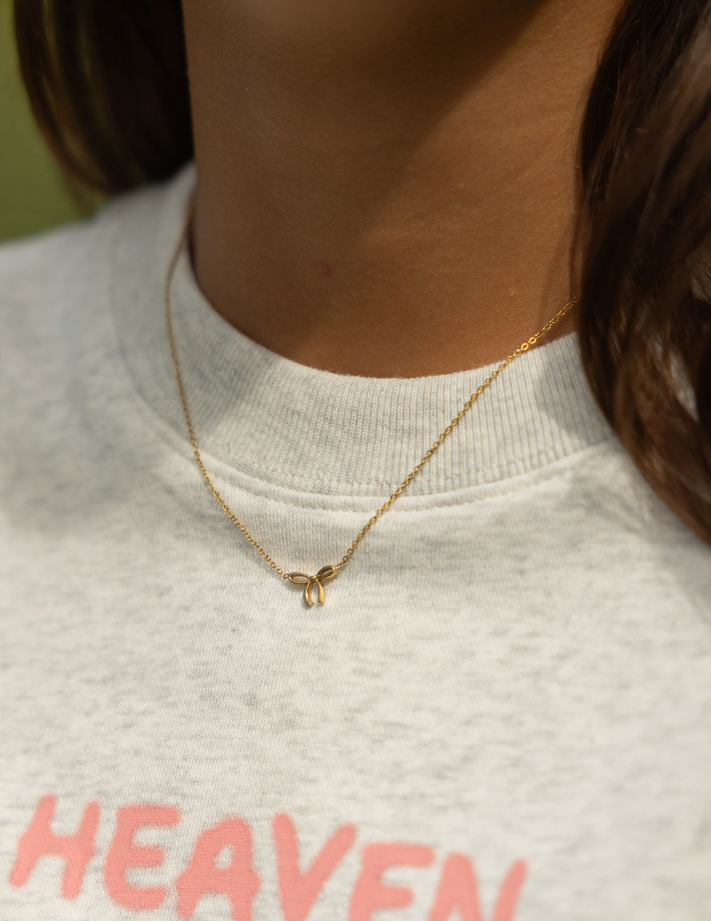 Dainty gold-tone bow necklace styled with a light grey graphic shirt