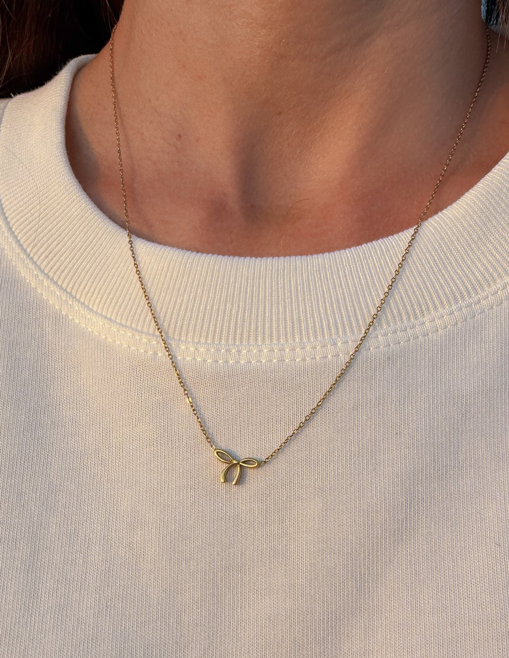 Dainty gold-tone bow necklace worn with a cream top