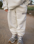 Deeply Loved Moonstone Kids Sweatpants with subtle lettering and gathered ankle cuffs, worn outdoors with sneakers