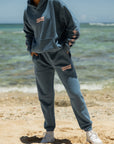 Model at the beach wearing Deeply Loved Stellar Blue Sweatpants styled with the matching hoodie