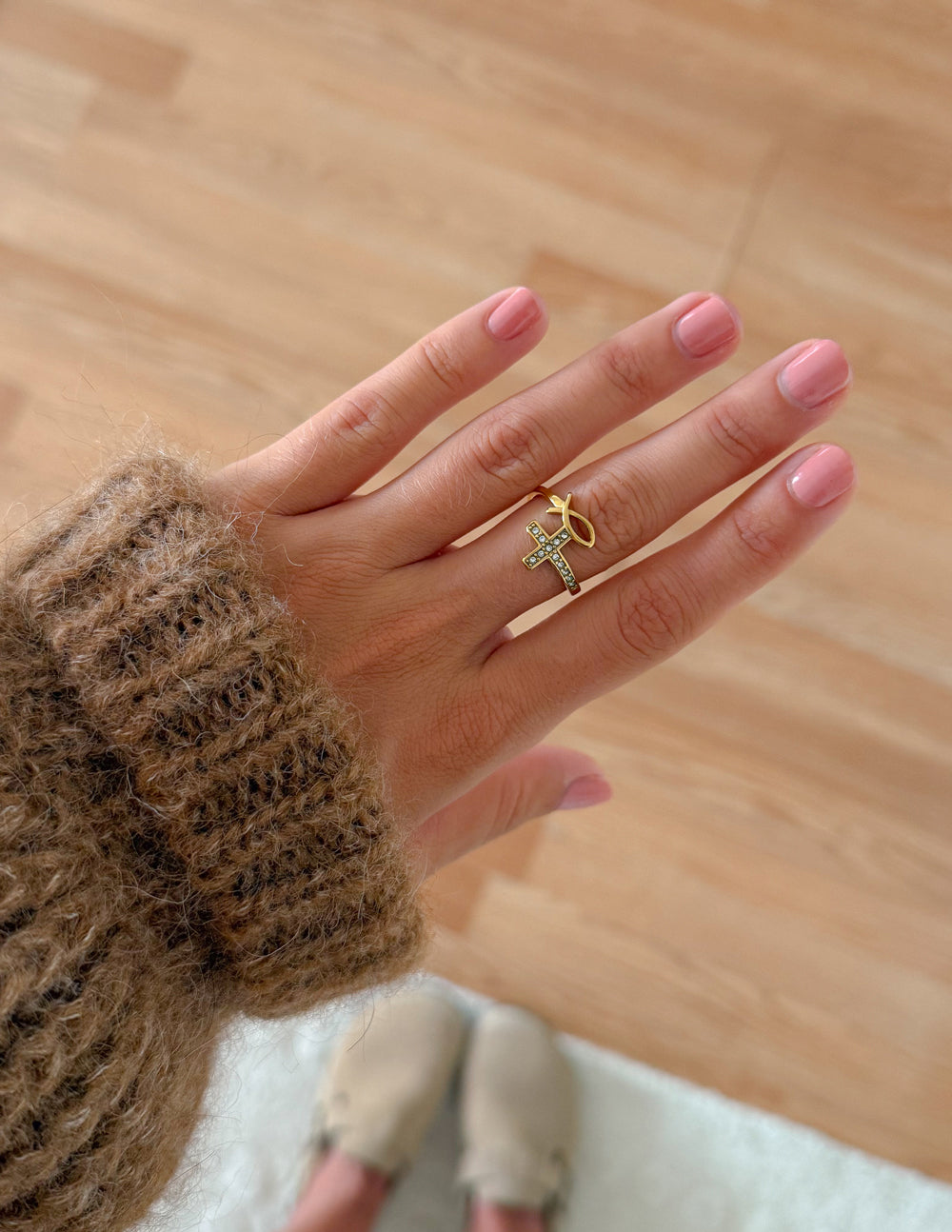 Devotion cross and fish ring worn with other gold-tone rings and a brown knit sleeve indoors