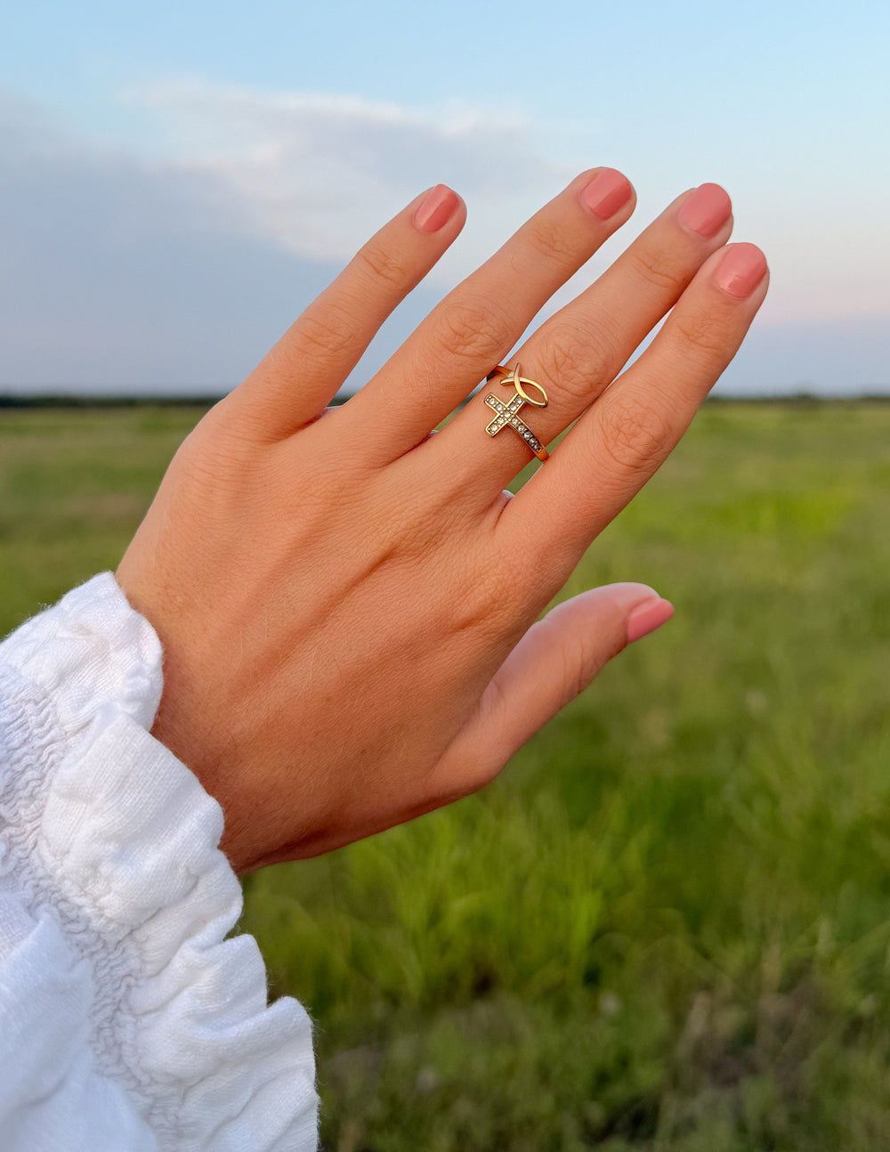 Devotion Ring styled with other rings on a hand against a green field and blue sky