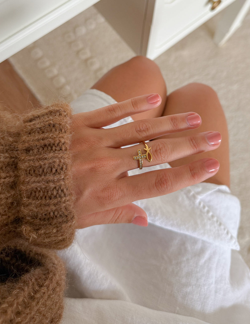 Devotion Ring worn with other rings beside white fabric and a brown knit sleeve