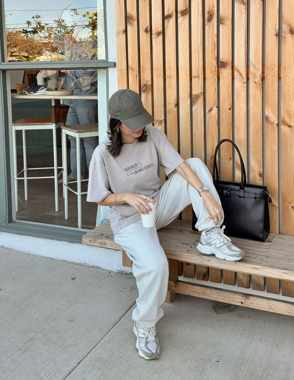 Model seated on a bench wearing the Chateau Grey Disciples Heavyweight Tee with light-colored pants