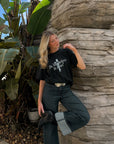 Woman posing beside a stone wall in the black Do You Believe in Jesus tee and dark jeans.
