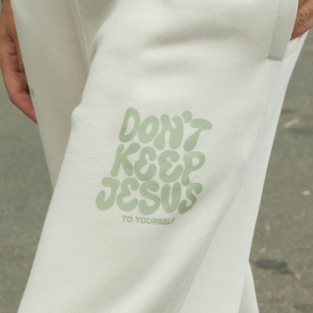 White sweatshirt with green text 'Don't Keep Jesus To Yourself' held by a person.