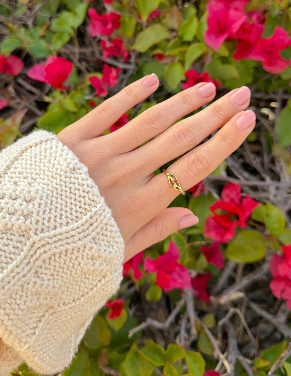 Eden gold-tone ring worn on a hand beside pink flowers with a cream knit sleeve