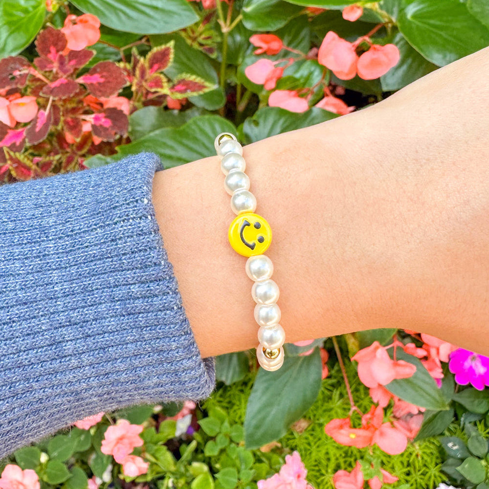 Pearl bracelet with a smiley face charm worn on a wrist against a floral background