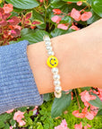 Pearl bracelet with a smiley face charm worn on a wrist against a floral background